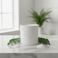 Still Water Eucalyptus & Sea Salt Soy Candle in a white ceramic jar on marble with eucalyptus branches